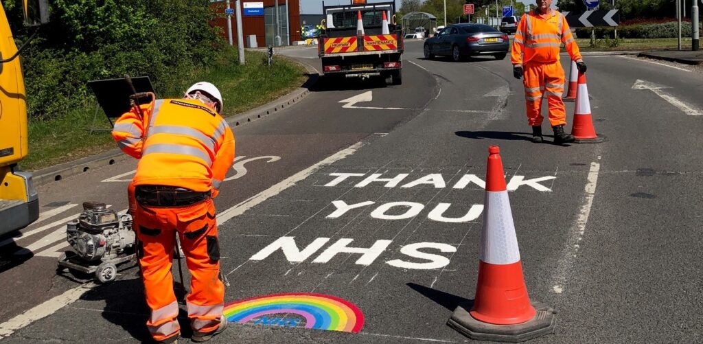 Road workers painting "Thank you NHS" on a road
